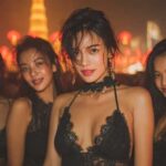 Four Asian women in black outfits at a Bangkok rooftop bar, illuminated by red lanterns.