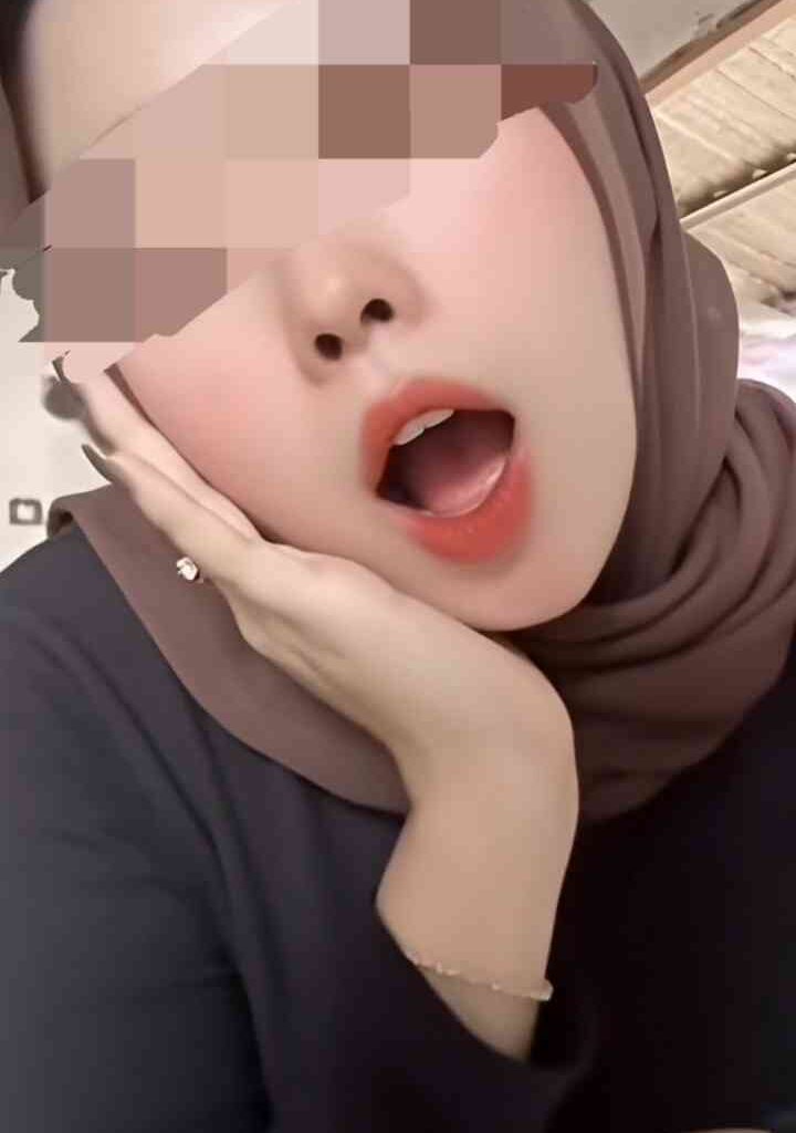 Young Malay woman in hijab, close-up of face with open mouth and hand on cheek.