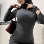Woman in a grey hijab and fitted dress holding a maroon handbag